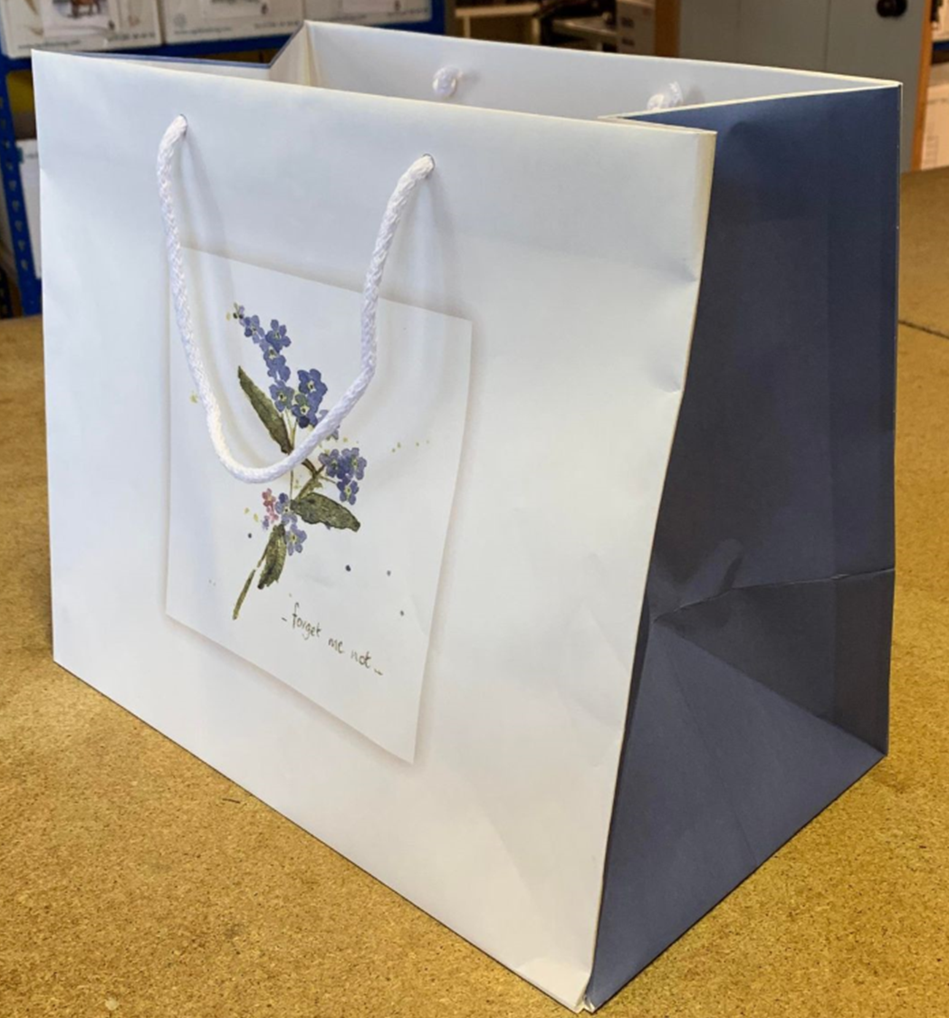 Pet casket bag with rope handle and forget me not print by Sarah Brown Cards on desk indoors